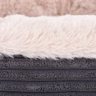 Gros plan sur un tissu à poils longs blancs et une base en tissu gris texturé, matériaux visibles d’un couchage ou accessoire pour animaux.
