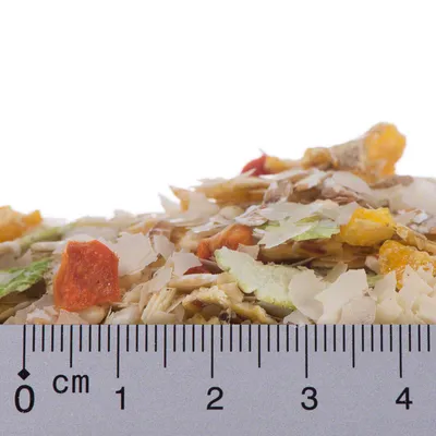 Zbliżenie na pokarm w płatkach z kawałkami warzyw, miarka pokazuje rozmiar do 4 cm.