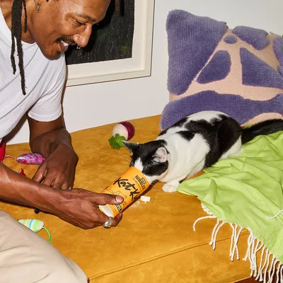 Person feeding a black and white cat directly from a tube of Kat-Kit paste, demonstrating product use for pets.