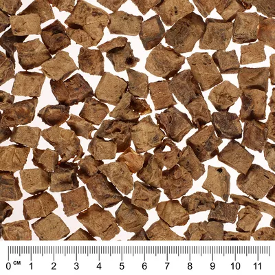 Lähikuva ruskeista, kuutionmuotoisista kuivalihapaloista, alhaalla senttimetrimitta. Näyttää palojen koon ja rakenteen.