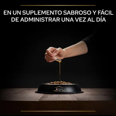 Mano vertiendo suplemento líquido sobre croquetas en un cuenco negro con el texto: En un suplemento sabroso y fácil de administrar una vez al día. Marca visible: Purina Pro Plan.