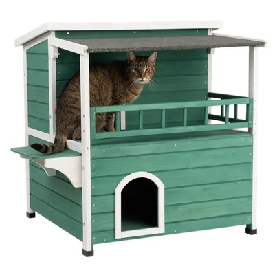 Casa per gatti in legno verde a due livelli con balcone coperto e ingresso. Gatto seduto sul balcone superiore.