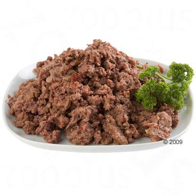 Nourriture humide pour animaux présentée sur une assiette blanche, garnie d'une branche de persil frais. Aucun emballage ou marque visible.