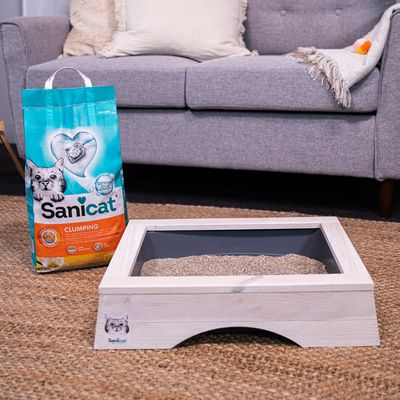 Sanicat Clumping cat litter with Oxygen Power, shown next to a wooden cat toilet on a carpet.