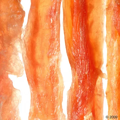 Nahaufnahme von getrockneten Fleischstreifen in orange-brauner Farbe, vermutlich als Snack oder Kauartikel für Haustiere.