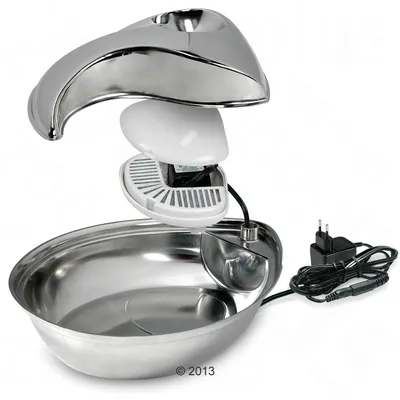 Stainless steel drinking fountain with removable filter and mains plug. Visible components: water tank, filter unit and power cable.