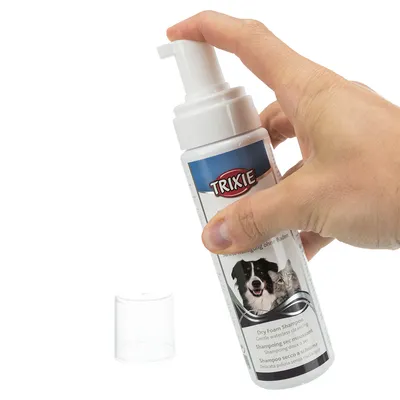 Trixie champú seco en espuma para perros y gatos, limpieza suave sin baño. Mano presiona el dispensador con la tapa quitada.