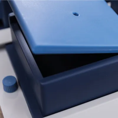 Boîte en plastique bleu marine avec couvercle bleu clair entrouvert, bouton rotatif visible sur le côté gauche. Aucun texte ou marque visible.