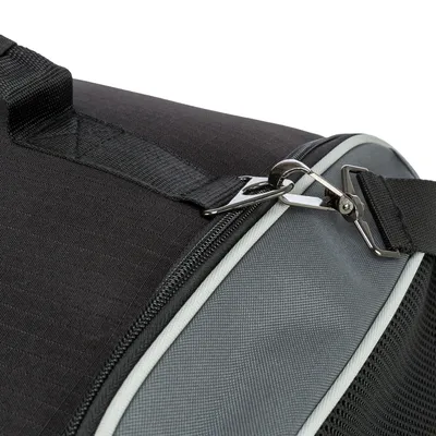Gros plan sur une fermeture éclair et une attache métallique d’un sac de transport en tissu noir et gris, avec sangle visible.