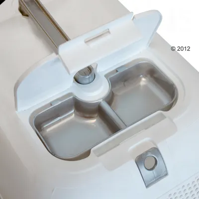 Nahaufnahme eines weissen Futterautomaten mit geöffnetem Deckel und zwei Edelstahl-Futterschalen. Nahaufnahme eines weissen Futterautomaten mit geöffnetem Deckel und zwei Edelstahl-Futterschalen.