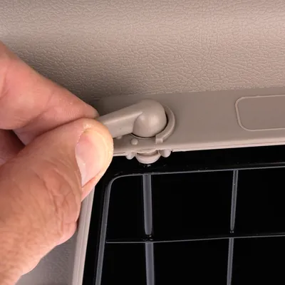 Fermeture en plastique beige d’une caisse de transport pour animaux, main ajustant le loquet près d’une grille noire visible en bas de l’image.