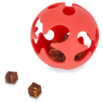 Röd leksaksboll från Nomad Tales med öppningar, fylld med små bruna godisbitar i kuber. Tre kuber ligger utanför bollen.