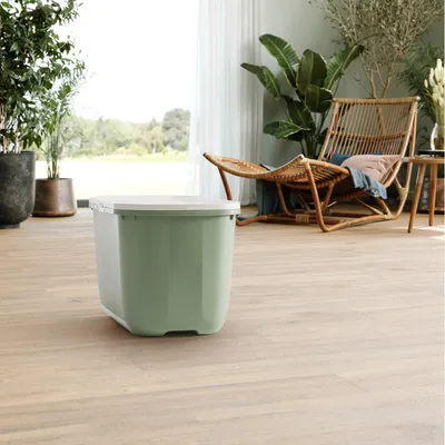 Green storage box with white lid, suitable for storing pet food or accessories. Shown in a modern living space with wooden floor and plants.