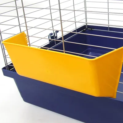 Bac à litière ou mangeoire jaune en plastique fixé sur la grille d'une cage bleue pour petits animaux, structure métallique visible.