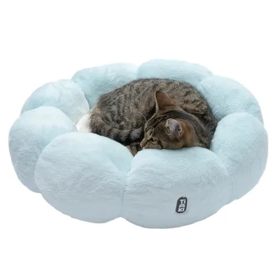 Light blue, round plush bed with Tiaki logo. A tabby cat is curled up inside.