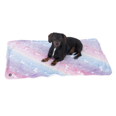 Куче лежи върху цветно одеяло с еднорог мотив и пастелни цветове.