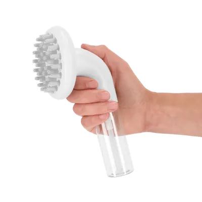 Hand håller en vit borste med plastborst och transparent handtag, lämplig för rengöring eller vård.