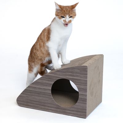 Chat roux et blanc debout sur un griffoir en carton marron en forme de rampe avec ouverture ronde sur le côté. Matériau visible : carton.