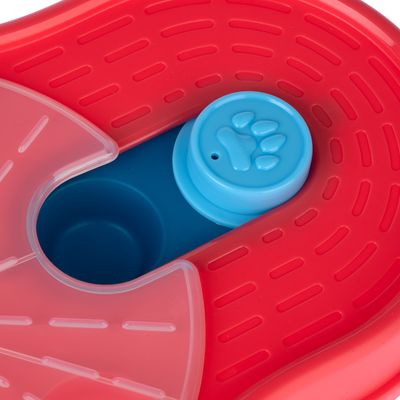 Vue rapprochée d’un jouet interactif en plastique rouge et bleu avec motif patte sur un bouton rond, parties transparentes visibles. Aucun texte ou marque apparente.