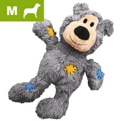 Gråt plyslegetøj formet som en bjørn med farvede lapper i blå og gul. M-symbol med hundesilhuet og bogstavet M øverst til venstre, indikerer størrelse til mellemstore hunde.