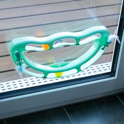 Zielona zabawka z żółtymi piłkami i piórami, przymocowana do szyby za pomocą przyssawek.