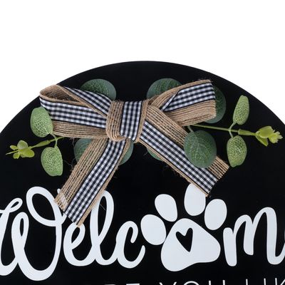 Texten "Welcome" med tassavtryck och hjärtsymbol, dekorerad med rutigt band och konstgjorda blad.