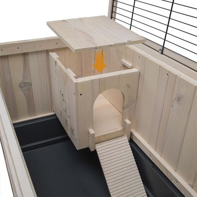 Casetta interna in legno con tetto rimovibile, rampa e incisione di coniglio su parete, all'interno di una gabbia per piccoli animali. Materiali visibili: legno e plastica.