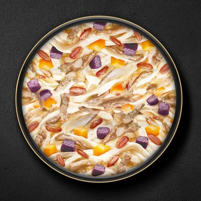 Assiette contenant des morceaux de viande blanche, cubes orange et violets, et petits morceaux rouges dans une sauce claire. Ingrédients visibles uniquement, sans marque apparente.
