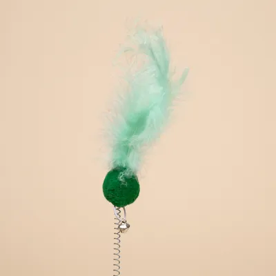 Boule verte avec plume turquoise fixée sur un ressort métallique, petit grelot argenté visible sous la boule. Jouet pour chat montré en gros plan.
