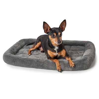 Malý pes leží na šedém, polstrovaném pelíšku pro domácí mazlíčky s měkkým povrchem.