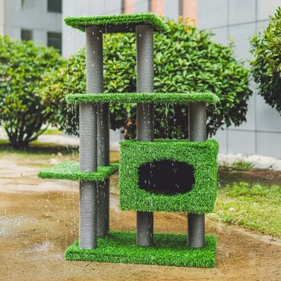 Kratzbaum mit grünem Kunstrasen, mehreren Ebenen und einer Höhle, im Freien unter Wasserstrahlen gezeigt.