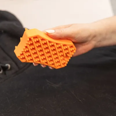 Hand houdt oranje borstel met nopjes vast, verwijdert haren van zwarte stof. Hand houdt oranje borstel met nopjes vast, verwijdert haren van zwarte stof.