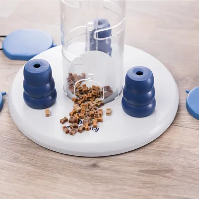 Speelgoed voor voeruitgifte met transparante container, blauwe elementen en kleine bruine snackstukjes op een witte basis.