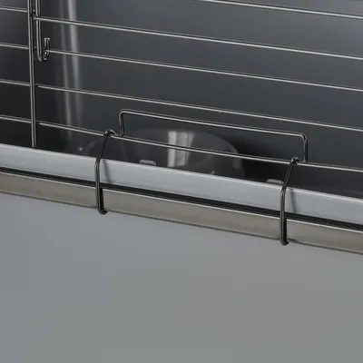 Detalje af bur med metalgitter og grå plastikbund, synlig skål indeni. Materialer: metal og plast.