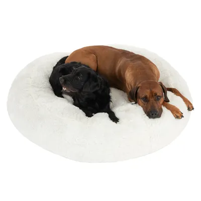To hunde ligger på en stor, rund, hvid hundeseng med blød plys. Sengen er egnet til flere hunde og viser rummelighed og komfort.
