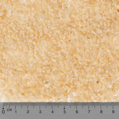 Gros plan sur litière minérale beige en petits grains, règle graduée de 0 à 9 cm visible en bas pour indiquer la taille des particules.