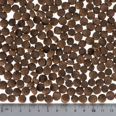Detailní záběr na hnědé granule suchého krmiva s měřítkem v centimetrech, ukazuje průměr granulí mezi 0,5 a 1 cm.