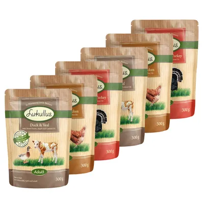 Pachete hrană umedă Lukullus 300 g, sortimente vizibile: Duck & Veal, Chicken, Turkey, cu imagini de animale pe ambalaj. Text în engleză pe fiecare pachet.