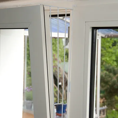 Grille de sécurité blanche en métal installée sur le côté d'une fenêtre oscillo-battante, fixée au cadre pour empêcher le passage dans l'ouverture.