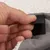 Detail van een hand die een zwarte klittenbandsluiting opent op grijze stof met witte fleecevoering, zichtbaar materiaal: textiel en klittenband.