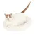 White cat with brown spots lying in a white, round cat bed made of soft material.