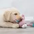 Pink soft toy in the shape of a rabbit with colourful ears and a white face, lying on a wooden floor.