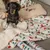 Tax med julstrumpor sitter på en filt med hundmotiv och granar, bredvid en kudde med broderad hund.