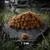 Haufen brauner Kroketten auf Stein, einzelne Krokette vorne mit Größenangabe 7-9 mm. Hintergrund zeigt Natur und eine Katze.