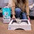 Litière pour chat Sanicat Clumping White 8L, sac visible à côté d’un bac à litière en bois, personne utilisant une pelle pour retirer un agglomérat.