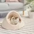 Cat cave made of beige fabric with soft padding, on a striped rug in a modern living room setting.