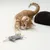 Chaton tigré orange jouant avec une souris en tissu gris à cordelettes, arrière-plan blanc, partie d’un autre chat noir visible à droite.