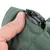 Közelkép zöld textil anyagról fekete cipzárral, amelyet egy kéz nyit ki.