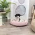 Hund liegt in einem rosa, plüschigen Haustierbett auf Holzboden. Dekorative Umgebung mit Pflanze und gerahmtem Bild im Hintergrund.