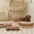 Braided dog basket with white cushion, next to it a wooden feeding station with two stainless steel bowls on a tiled terrace.